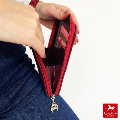 Carteira vermelha com fecho e vários compartimentos, interior castanho, em mão sobre calças de ganga