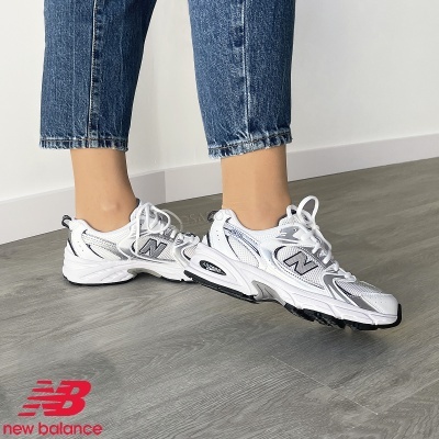 Ténis desportivos brancos New Balance com detalhes cinzentos em piso cinzento