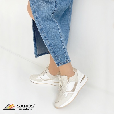 Ténis brancos e cinzentos em fundo branco com pessoa vestindo calças de ganga azuis