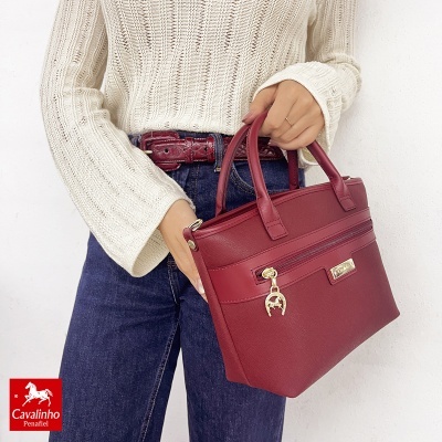 mulher com camisola bege e calças de ganga segurando mala de mão vermelha