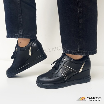 Ténis pretos de cunha com atacadores e detalhe de tachas ao lado, usados com calças pretas.