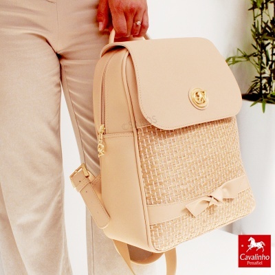 Mochila bege com textura trançada e fecho dourado, com laço decorativo
