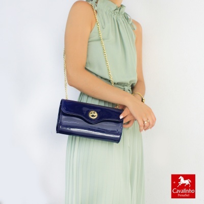 Mala azul escuro com alça corrente dourada usada por mulher com vestido verde claro