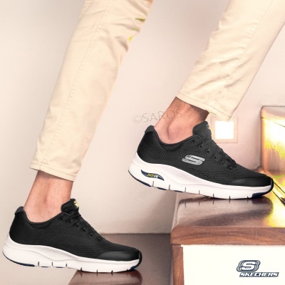 Sapatos Skechers pretos com sola branca e detalhes amarelos usados numa escada interior