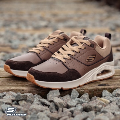 Sapatilhas Skechers castanhas com sola branca e castanha em chão de pedra