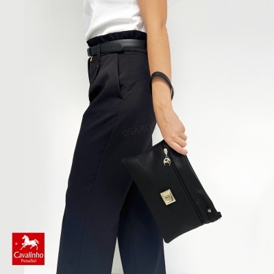 Pessoa com calças pretas e clutch preta contra fundo branco com logótipo Cavalinho Penafiel