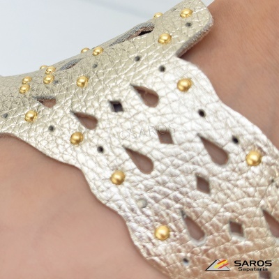 Pulseira de couro prateado com tachas douradas num pulso
