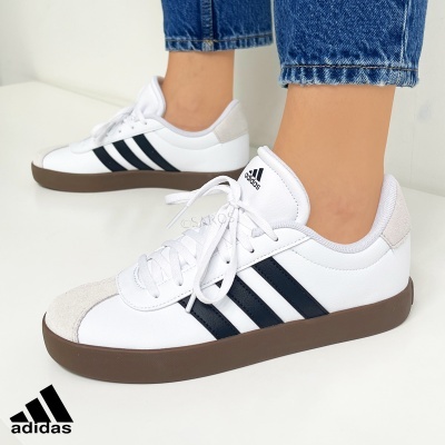 Ténis Adidas brancos e pretos com sola castanha e material cinzento claro na frente.