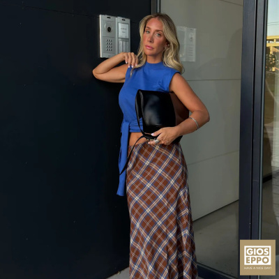 Mulher com blusa azul sem mangas e saia padrão xadrez castanha com bolsa preta