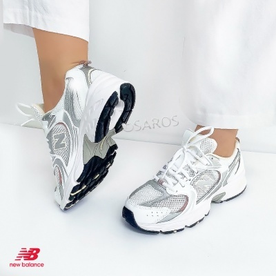 Ténis New Balance branco e prateado com solado preto, destacados num fundo branco.