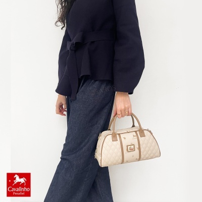 Mala bege e castanha Cavalinho com padrão de cavalinhos e textura acolchoada junto a mulher com roupa preta e jeans