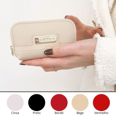 Carteira pequena bege com placa metálica Cavalinho e fecho ziper segurada por mãos femininas