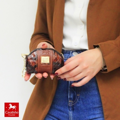 Carteira pequena castanha em couro com aplique dourado e corrente, segurada por pessoa vestida casual