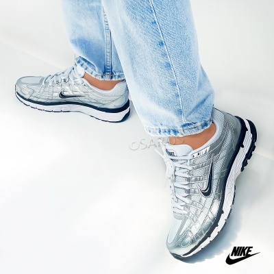 Ténis Nike prateados e cinzentos com sola branca e preta usados por pessoa com calças de ganga claras