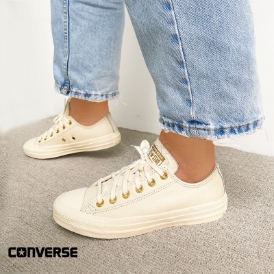 Ténis Converse Star creme com detalhes dourados usados com jeans azuis