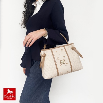 Mala bege e castanha com padrão e logótipo Cavalinho, usada por mulher com roupa preta e branca