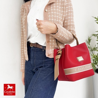Mala vermelha Cavalinho com alça castanha e pessoa vestindo camisa branca, casaco bege e calças de ganga azuis