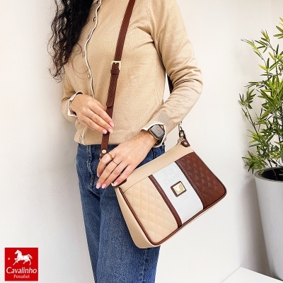 Mala de ombro Cavalinho Penafiel bicolor com padrão matelassê, em ambiente interior com parede branca e planta verde.