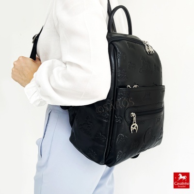 Mala mochila preta com textura de cavalos e fechos prateados usada por pessoa com camisa branca e calças azul claro