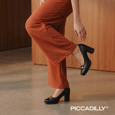 Sapatos pretos de salto grosso com aplicação dourada usados com calças largas castanho-avermelhadas em ambiente interior