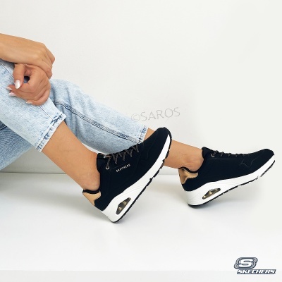 Ténis Skechers pretos e castanhos com sola branca, em fundo branco