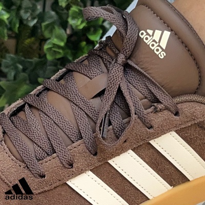 Ténis adidas castanhos com riscas brancas e logo visível