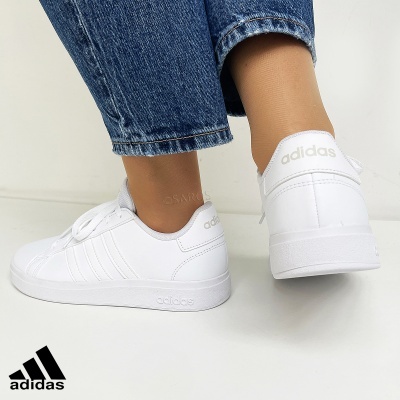Ténis Adidas brancos usados com calças de ganga azuis sobre fundo branco