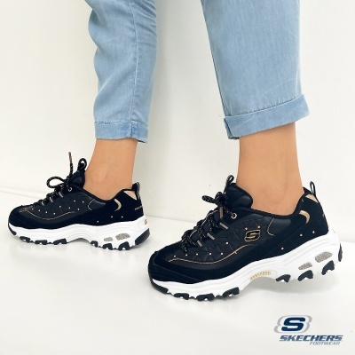 Ténis pretos Skechers com sola branca e detalhes dourados usados numa pessoa com calças de ganga claras