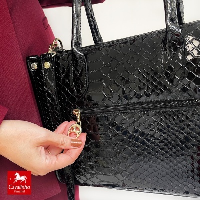Mala preta brilhante com padrão de pele de crocodilo e puxador dourado em forma de ferradura.