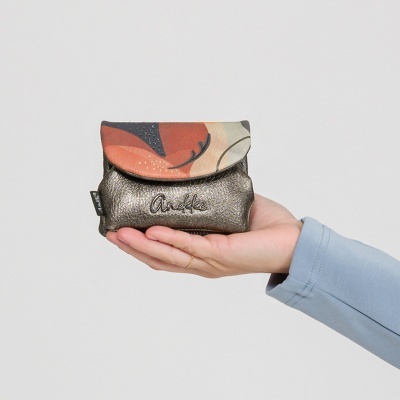 Carteira pequena metalizada bronze com aba floral colorida e nome Anekke bordado, segurada por mão com manga azul.