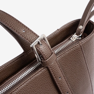 Detalhe de mala castanha de pele com fecho metálico e alça ajustável