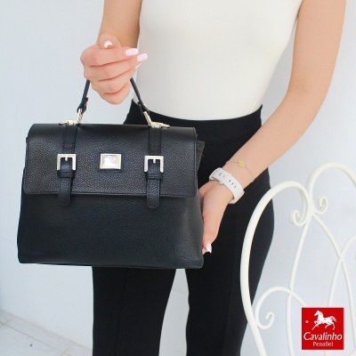 Mala de mão preta em couro com fivelas prateadas segurada por mulher