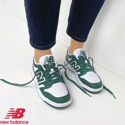 Ténis New Balance 480 brancos e verdes com atacadores verdes usados por pessoa com jeans, em fundo branco