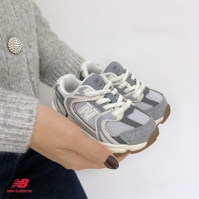 Ténis infantis New Balance cinzentos e brancos na mão de uma pessoa com camisola cinzenta