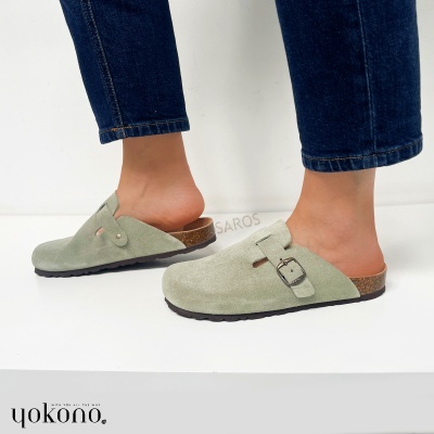 Chinelos tipo mule em camurça verde clara com fivela metálica, sola preta e palmilha de cortiça, usado com calças de ganga azul