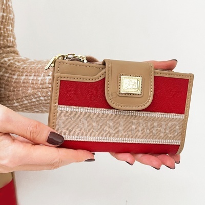 Carteira vermelha e bege com texto Cavalinho e placa dourada, segurada por mãos femininas.