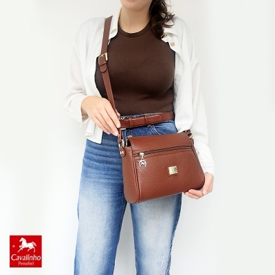 Mulher com mala transversal castanha em pele e cinto combinando com jeans