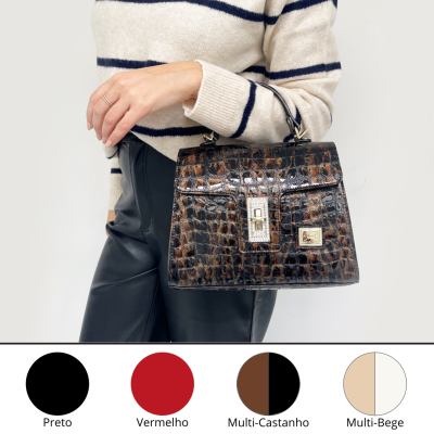 Mala de mão castanha com padrão de pele de crocodilo e fecho dourado, com pessoa vestindo camisola bege às riscas pretas e calças pretas