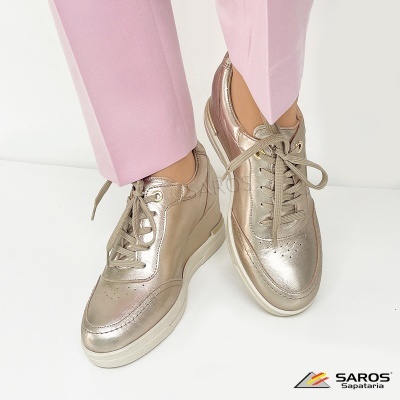 Tênis metálicos dourados com atacadores e solas brancas usados com calças rosas.