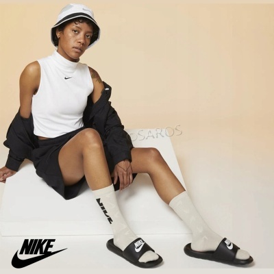 Mulher com roupa desportiva e crocodos Nike pretos num fundo bege e branco