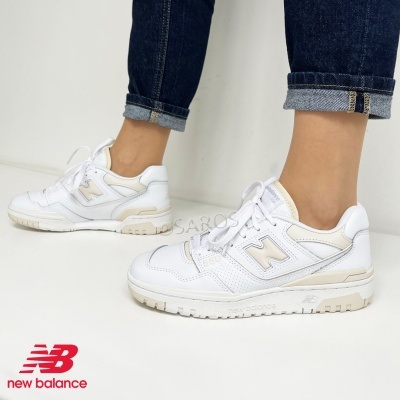 Tênis New Balance brancos com detalhes bege usados com jeans escuro.