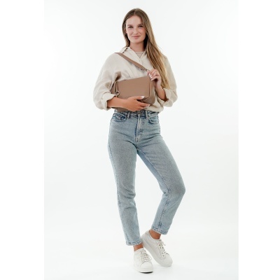 Mulher com jeans azuis, camisa creme, ténis brancos e uma mala bege de pele
