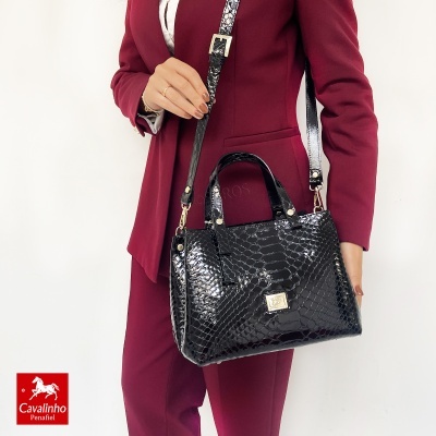 Mala preta padrão pele de crocodilo mostrada numa modelo com fato vinho