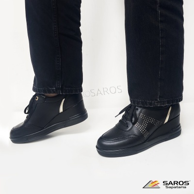 Ténis pretos de couro com tachas metálicas e detalhes brancos, usados com calças pretas