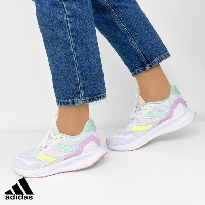 Ténis desportivos Adidas em tons pastel com sola branca e detalhes coloridos, usados com calças de ganga azuis.