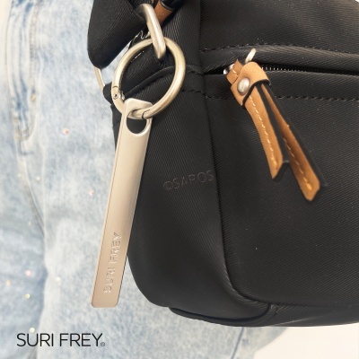 Saco preto em tecido com detalhes em pele castanha e metal prateado, com logo SURI FREY, sobre fundo de jeans azul claro