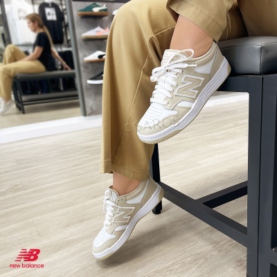 Ténis New Balance branco e bege usados por pessoa com calças bege sentada.
