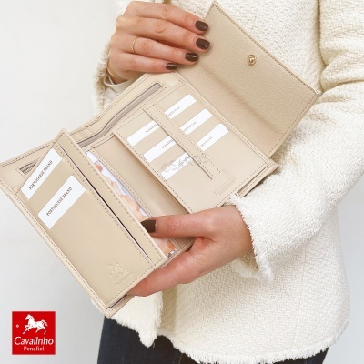 Carteira bege em couro com vários compartimentos para cartões aberta nas mãos de pessoa com casaco branco