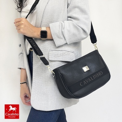 Carteira preta Cavalinho com alça preta e dourada, usada por pessoa com casaco cinza claro