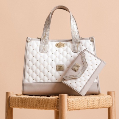 Mala e carteira brancas matelassé com detalhes bege e fechos dourados sobre banco de madeira.